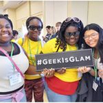 Four girls of color holding Geek is Glam sign at our STEM Expo Event for Girls