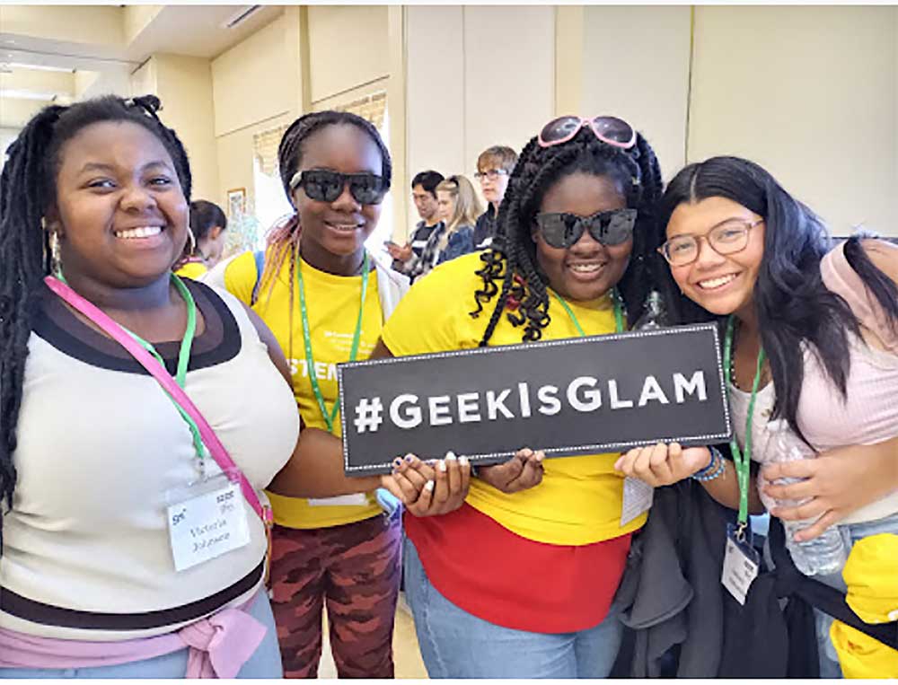 Four girls of color holding Geek is Glam sign at our STEM Expo Event for Girls